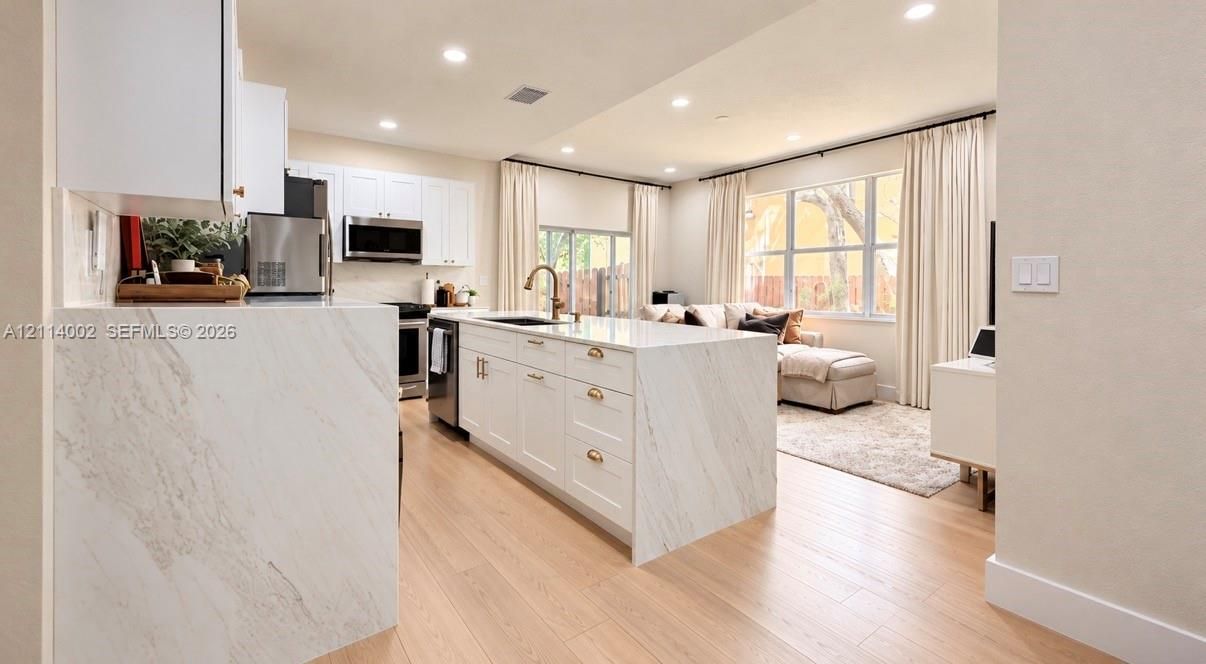 Kitchen featuring a waterfall-edge stone countertop, shaker-style cabinetry, stainless steel appliances, and wood-finish flooring