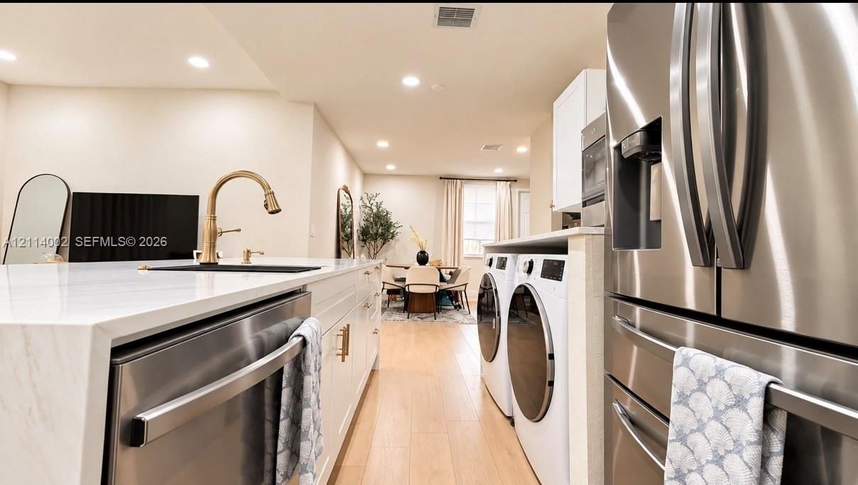 Kitchen featuring a stone-surface island, stainless steel appliances, recessed lighting, and wood-finish flooring, with an integrated laundry area