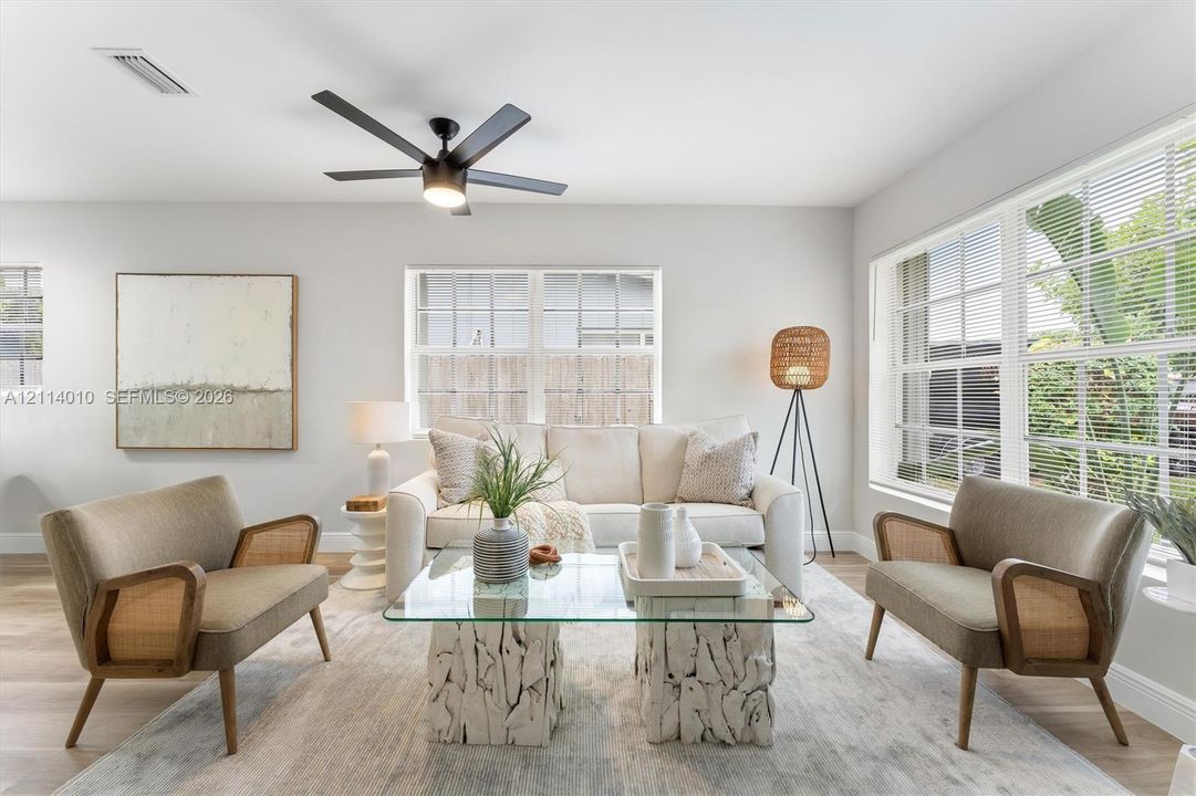 Light-filled interior featuring expansive multi-pane windows, wood-finish flooring, and a central matte black ceiling fan with integrated lighting