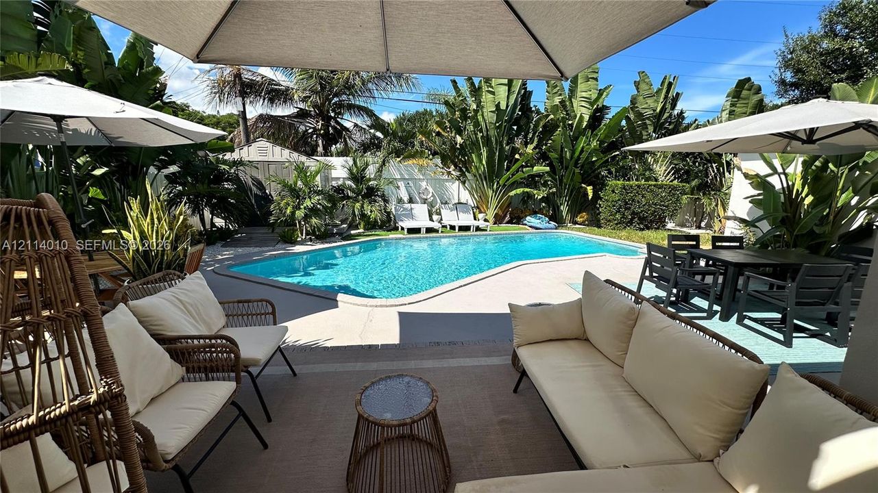 Outdoor living area featuring a concrete patio, swimming pool with concrete surround, and tropical landscaping