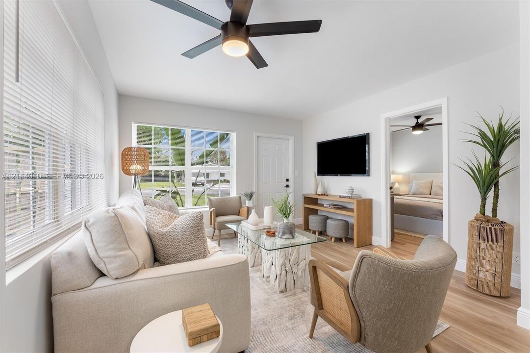 Living area featuring wood-finish flooring, a contemporary ceiling fan with integrated lighting, and multi-pane windows with horizontal blinds
