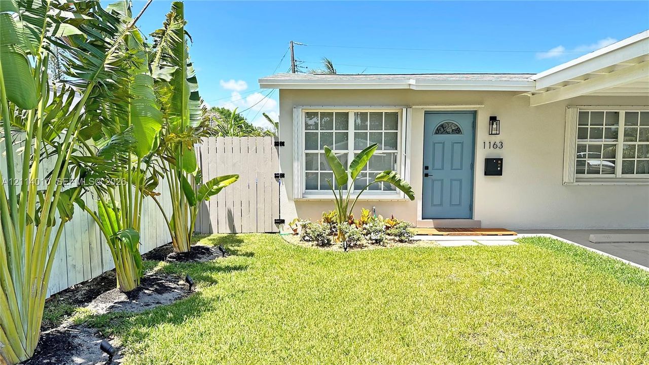Exterior featuring light-toned stucco siding, a blue painted entry door, grid-pattern windows, an attached carport, and a fenced perimeter