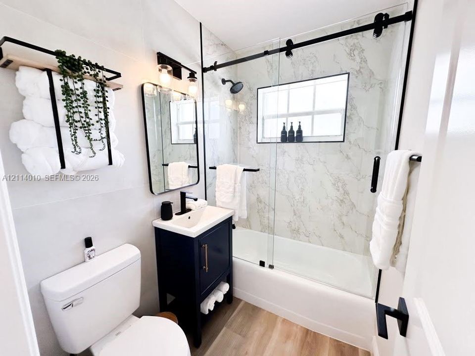 Bathroom featuring a vanity with a rectangular sink, stone-patterned shower surround, glass sliding shower door with matte black hardware, and wood-finish flooring