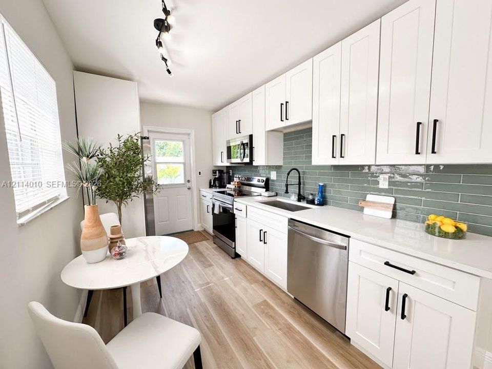 Kitchen featuring white shaker-style cabinetry, solid-surface countertops, subway-style tile backsplash, stainless steel appliances, and wood-finish flooring