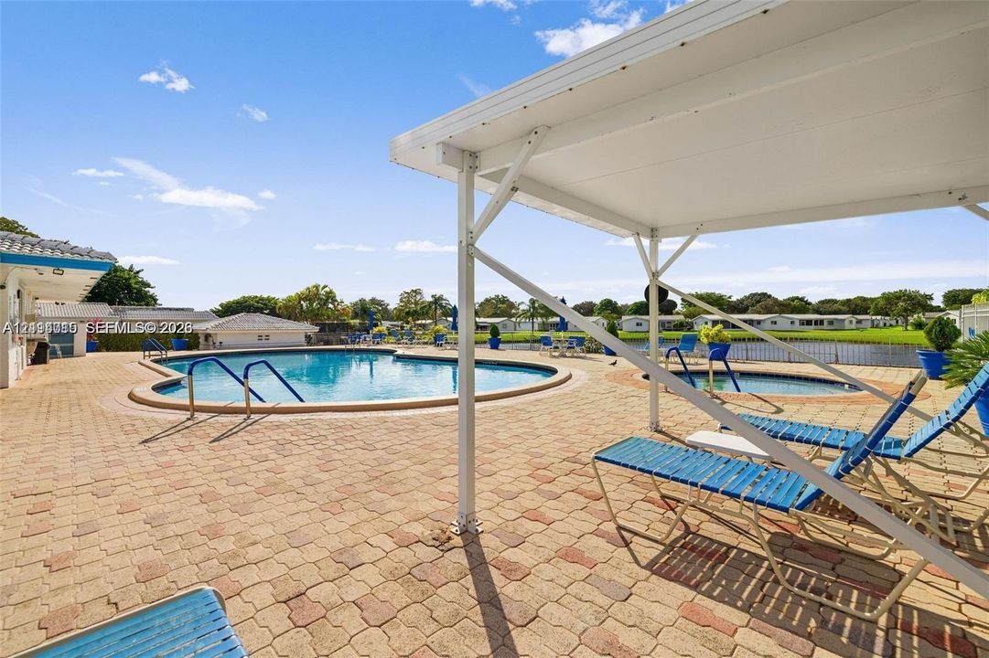 Outdoor swimming pool and spa area featuring a paved brick patio, covered pavilion, and water-side perimeter fencing