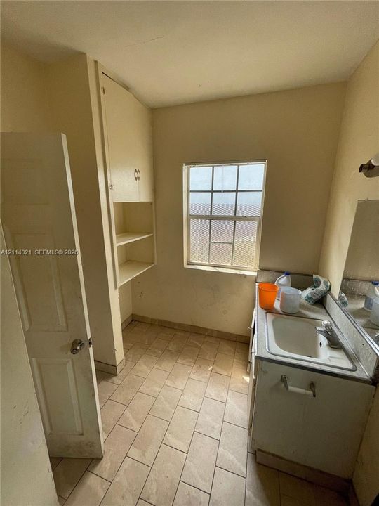 Utility room featuring ceramic tile flooring, built-in cabinetry with open shelving, a single-basin drop-in sink, and a grid-pattern window