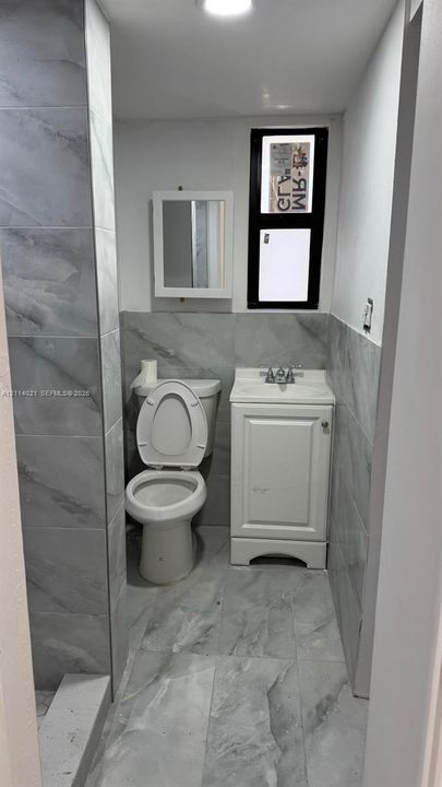Bathroom featuring full-height large-format stone-patterned tile wall cladding, porcelain floor tiling, white single-door vanity with integrated basin, and wall-mounted medicine cabinet