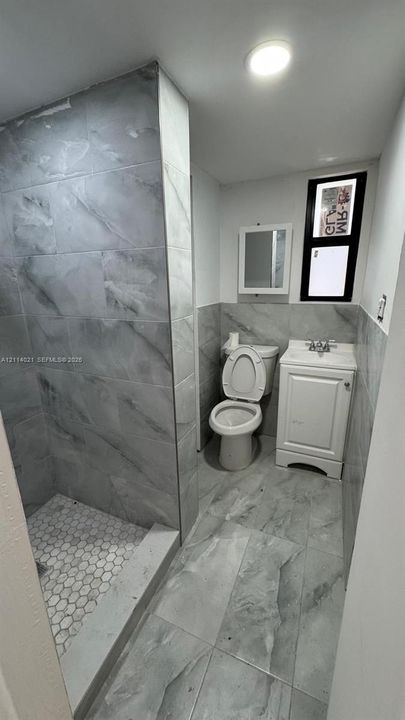 Bathroom featuring large-format gray tile flooring and shower surround, a walk-in shower with hexagonal floor tiling, a white vanity with an integrated basin, and a wall-mounted medicine cabinet