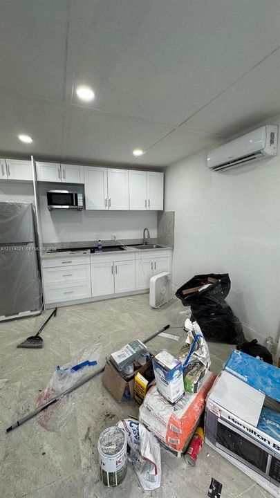 Kitchen featuring white shaker-style cabinetry, stone-finish countertops, stainless steel sink with pull-down faucet, wall-mounted ductless climate control unit, and recessed ceiling lighting