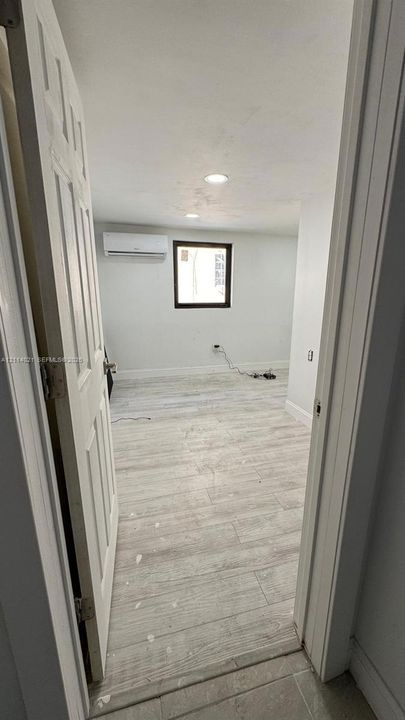Room featuring light wood-finish flooring, a wall-mounted ductless mini-split system, recessed ceiling lighting, and a window with a dark frame