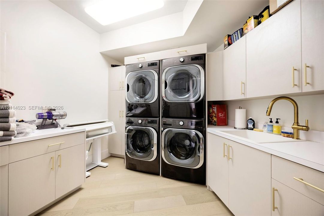 Custom cabinetry with brass-finish hardware, dual stacked laundry units, solid-surface countertops, integrated utility sink with brass-finish faucet, and wood-finish flooring