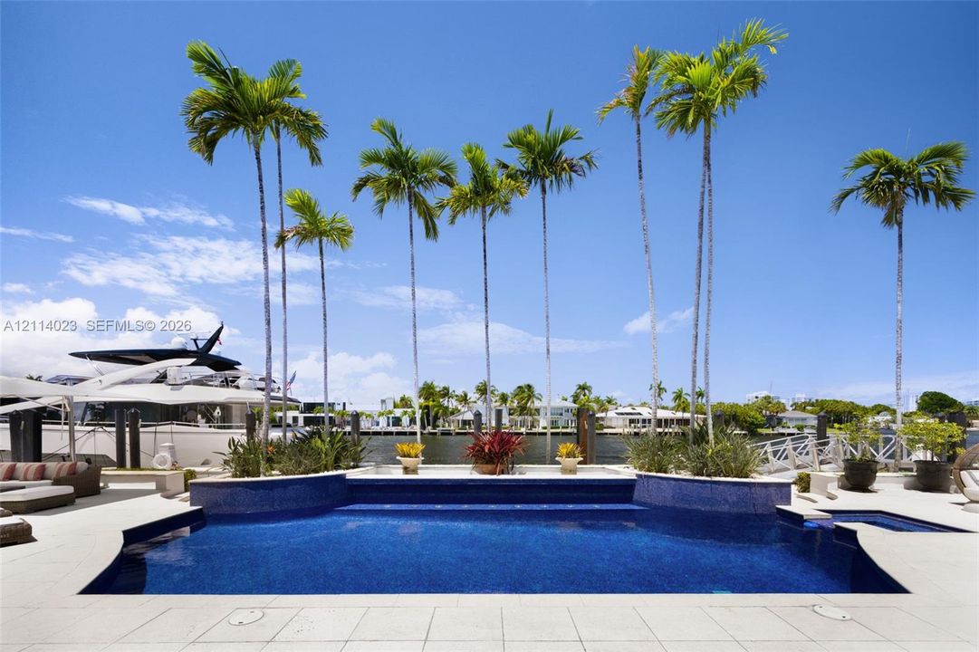 Waterfront pool featuring a mosaic-tile finish, elevated spa, stone-paver decking, and manicured palm tree landscaping