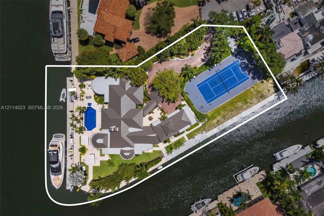 Waterfront estate featuring a private deep-water dock, tennis court, swimming pool, and expansive hardscaped grounds with mature landscaping