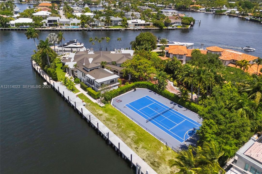 Waterfront estate featuring a private deep-water dock, multi-purpose sport court, extensive shoreline footage, and mature tropical landscaping