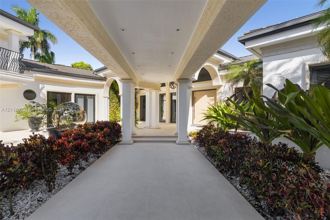 Covered grand entrance featuring structural columns, recessed lighting, and stone-tile flooring, framed by manicured landscaping