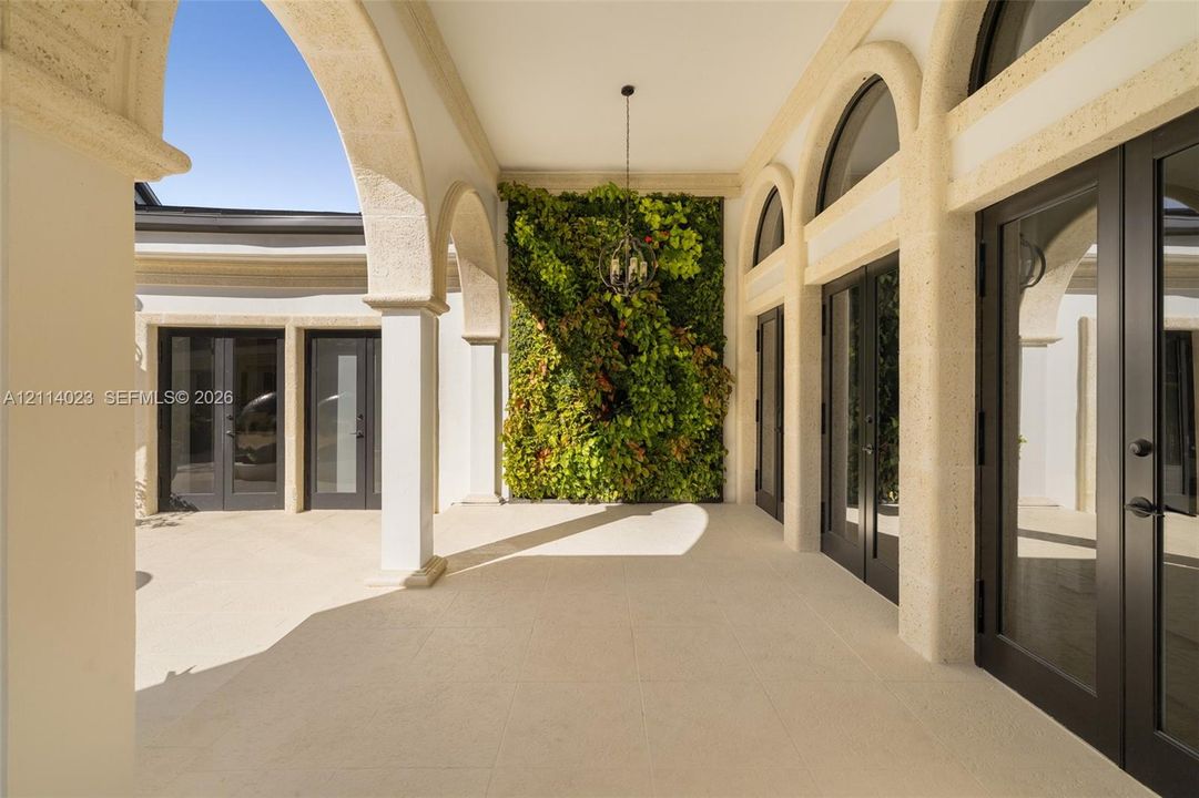 Covered patio featuring stone-finish arched colonnades, large-format stone flooring, a vertical garden wall, and multiple sets of dark-framed glass paneled doors