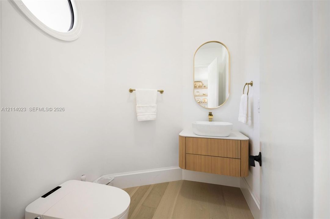 Floating wood-finish vanity with a vessel sink, oval wall mirror, wall-mounted hardware, and circular accent window