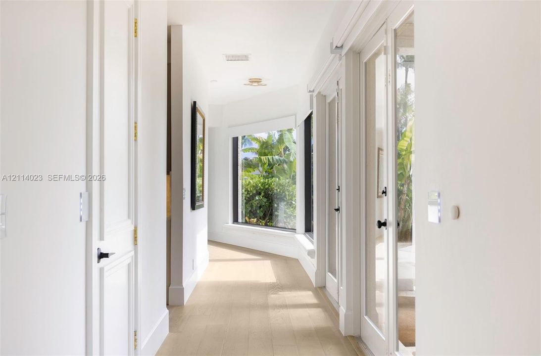 Hallway featuring wood-finish flooring, crisp white wall finishes, a large bay window, and glass-paned doors with matte black hardware