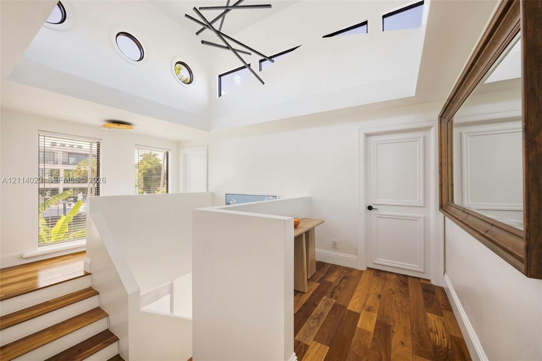 Vaulted ceiling featuring multiple clerestory and circular windows, wood-finish flooring, and modern geometric chandelier