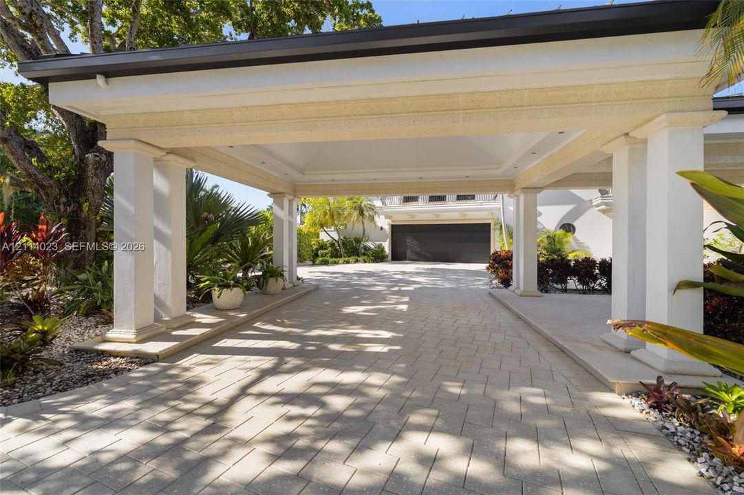 Covered porte-cochere featuring structural columns, recessed lighting, and a paved stone driveway leading to a multi-car garage