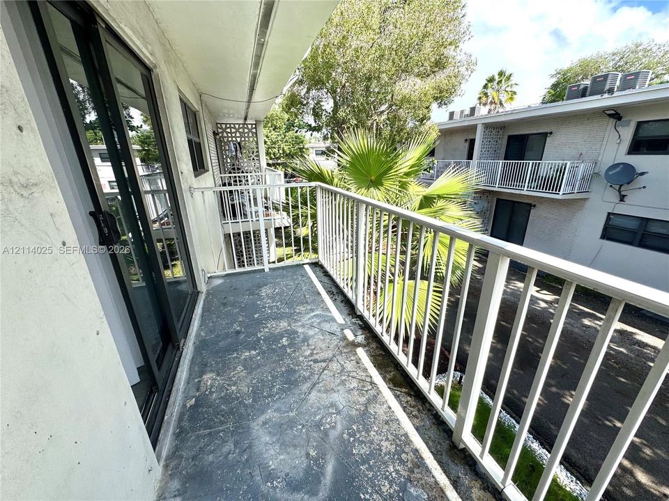 Covered balcony featuring white metal railings, sliding glass door, and solid surface flooring
