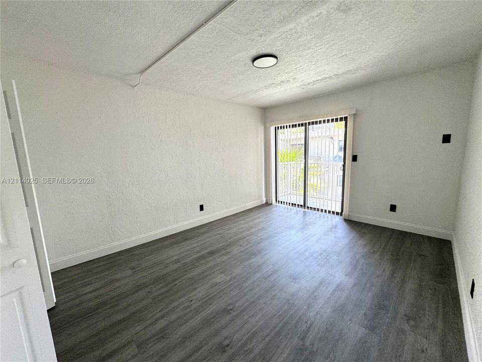 Room featuring wood-finish flooring, textured wall surfaces, and a sliding glass door with vertical blinds