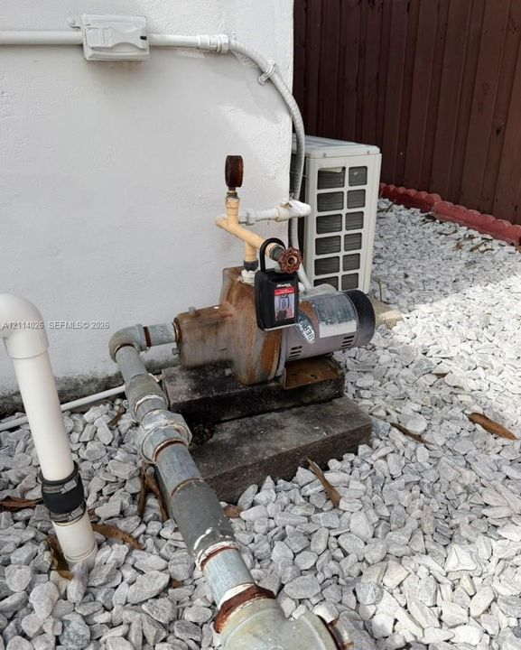 Exterior utility area featuring a water pump system, HVAC condenser unit, and crushed stone ground cover