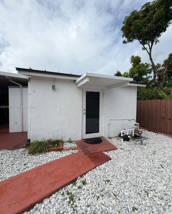Exterior area featuring white stucco siding, a paved walkway, light-toned stone ground cover, and a covered entryway
