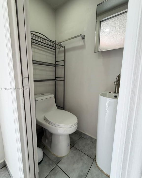 Compact restroom featuring a white pedestal sink with a single-handle faucet, a one-piece elongated toilet, and grey tile flooring