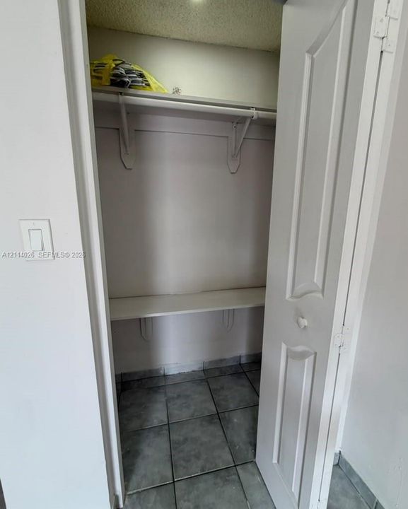Storage closet featuring tile flooring, two-tiered built-in shelving, and a paneled door