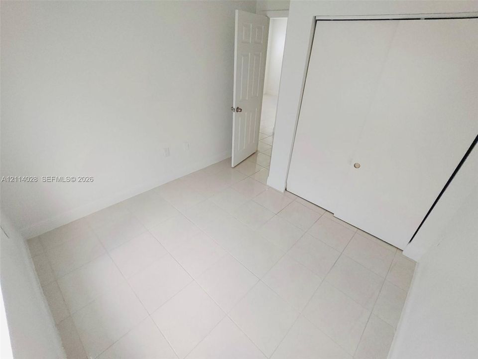 Interior space featuring white-toned tile flooring, neutral walls, a six-panel door, and a built-in closet with sliding doors
