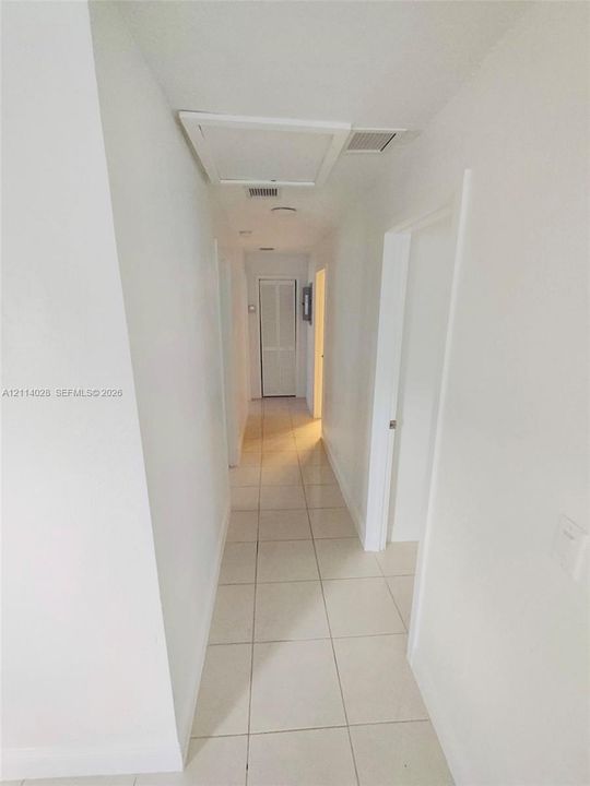 Hallway featuring large-format ceramic tile flooring, neutral wall finishes, recessed lighting, and louvered closet doors