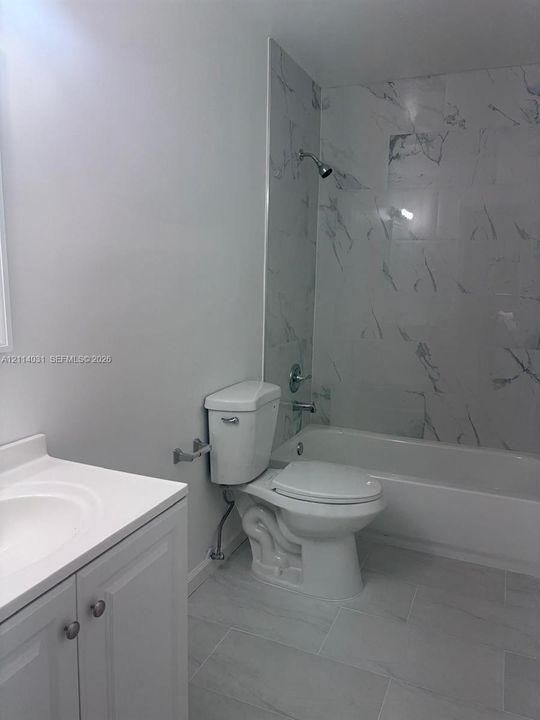 Bathroom featuring large-format tile flooring, vanity with integrated basin, and full-height tiled tub surround