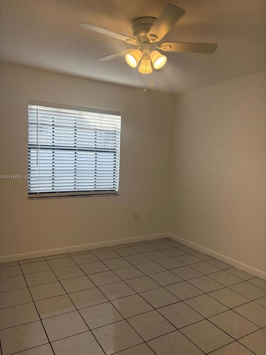 Interior space featuring neutral wall paint, tile flooring, a window with installed horizontal blinds, and a ceiling fan with integrated lighting