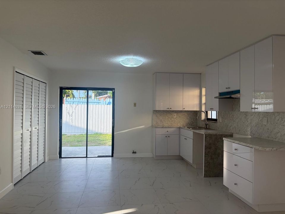 Kitchen featuring high-gloss white cabinetry, stone-patterned countertops, coordinating backsplash, large-format tile flooring, and sliding glass doors