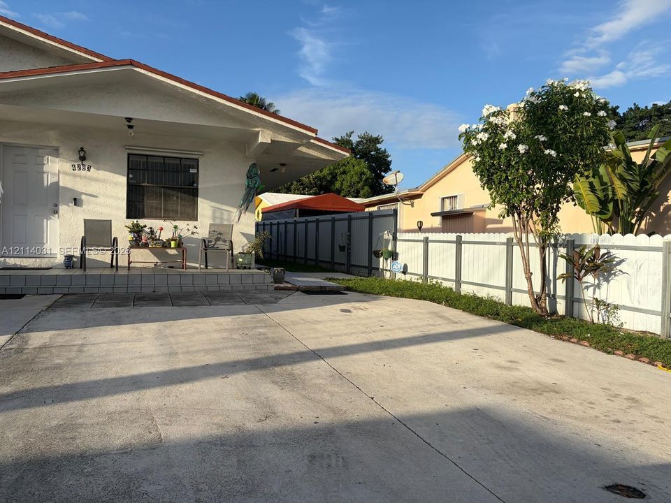 Stucco exterior residence featuring a tiled front porch, concrete driveway, and white picket-style fencing