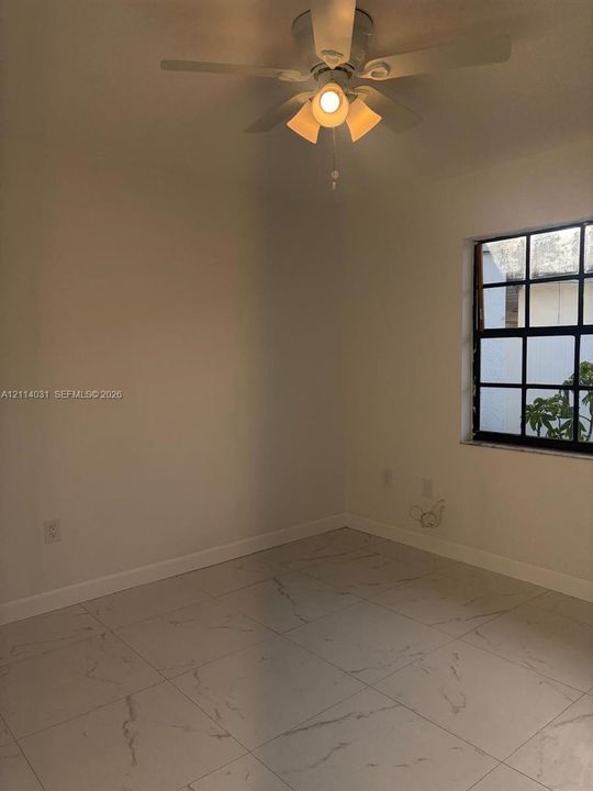Neutral-toned interior featuring large-format tile flooring with subtle veining, multi-pane grid window, and a ceiling-mounted light fixture with a central fan