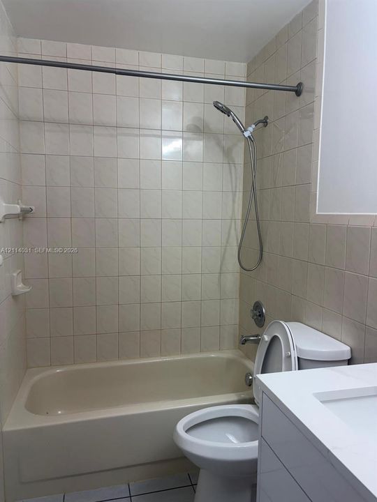 Full bathroom featuring a tub-shower combination with square wall tile, a hand-held shower fixture, a vanity with a white countertop and integrated sink, and tile flooring