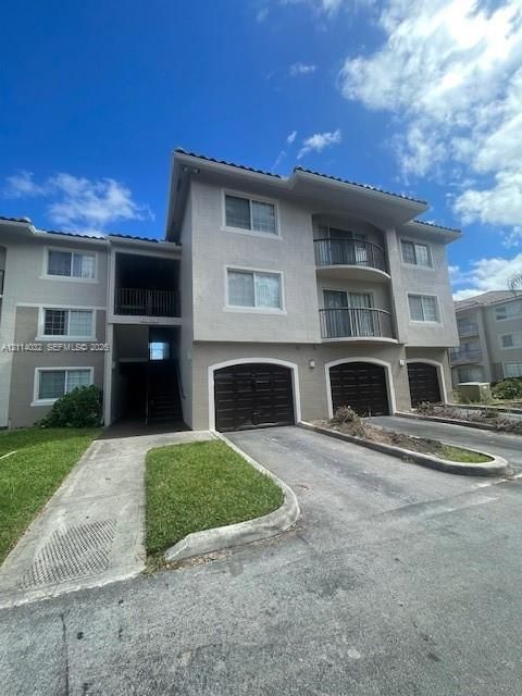 Multi-story exterior featuring a stucco facade, private garage bays with arched detailing, and stacked balconies with metal railings
