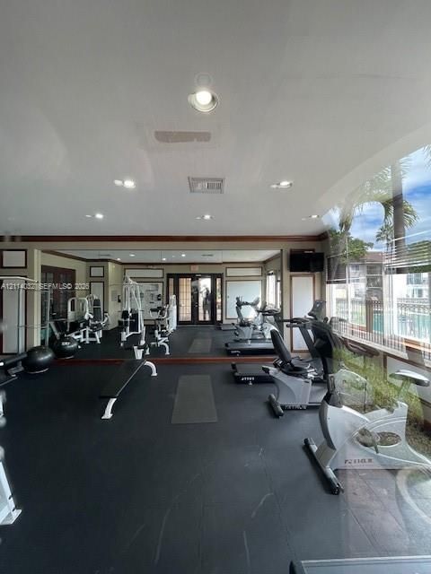 Fitness room featuring impact-resistant rubber flooring, floor-to-ceiling wall mirrors, recessed lighting, and large windows