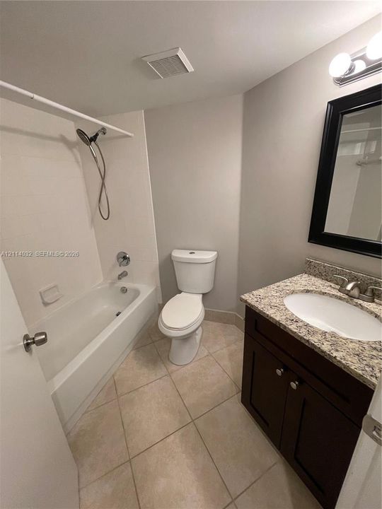 Bathroom featuring a dark wood vanity with a stone countertop, an integrated porcelain sink, tile flooring, and a shower-tub combination