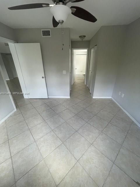 Neutral-toned interior space featuring light-colored diagonal floor tiling, a ceiling fan with integrated lighting, and multiple interior doorways