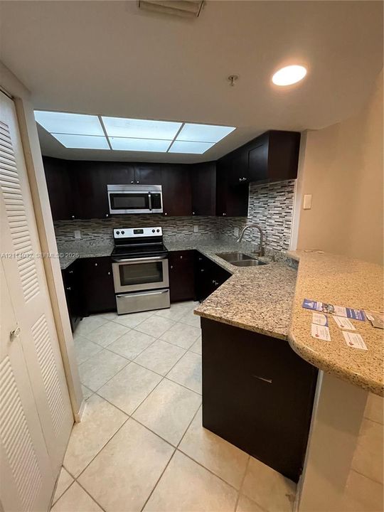 Kitchen featuring dark cabinetry, stone-finish countertops, stainless steel appliances, a multi-tone tile backsplash, and tile flooring