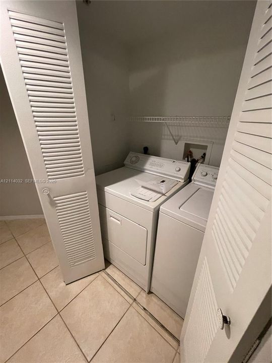 Laundry closet featuring white louvered doors, tile flooring, and integrated wire shelving