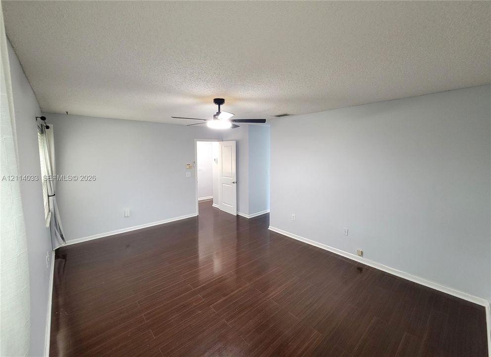 Room featuring dark-toned wood-finish flooring, a central ceiling fan with integrated lighting, and a multi-panel interior door