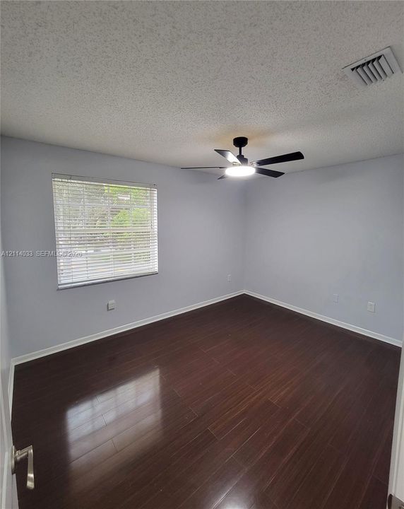 Room featuring dark wood-finish flooring, neutral wall paint, and a ceiling-mounted light fixture with an integrated fan