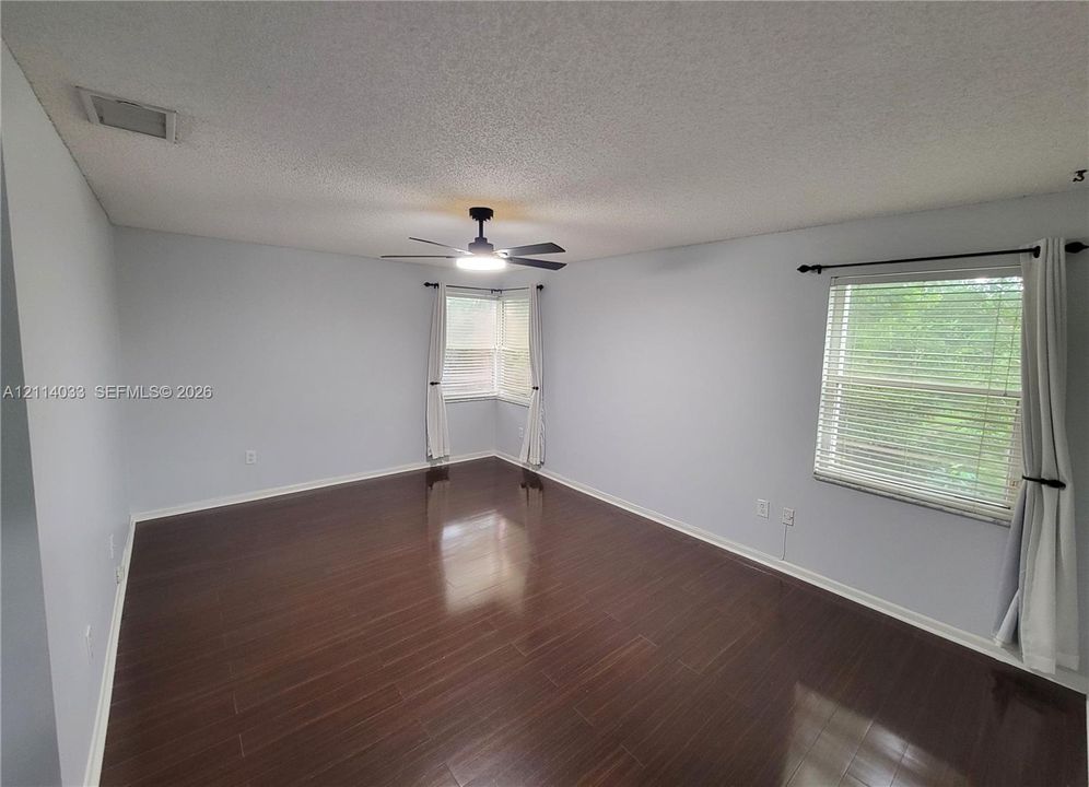 Interior space featuring dark wood-finish flooring, a ceiling fan with integrated lighting, dual-window corner configuration, and horizontal window blinds