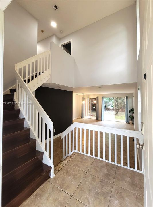 Foyer featuring high ceilings, wood-finish staircase treads, white balustrades, large-format tile flooring, and sliding glass doors