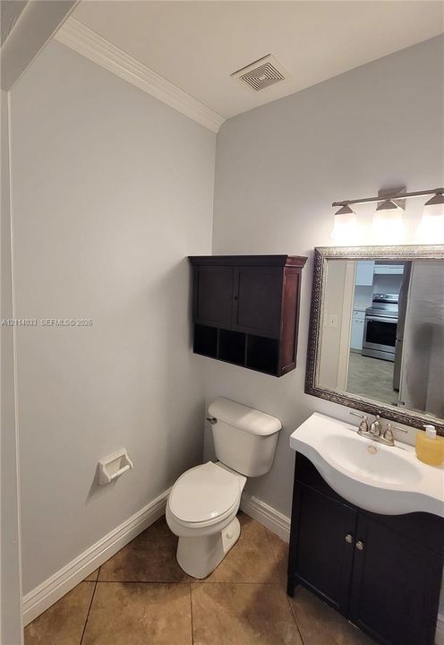 Vanity with a molded sink, dark wood-finish cabinet, wall-mounted storage unit, three-bulb vanity light fixture, and tile flooring