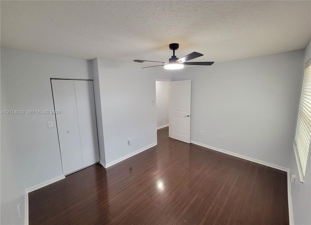 Room featuring dark wood-finish flooring, a matte black ceiling fan with an integrated light fixture, a bi-fold closet, and a white interior door